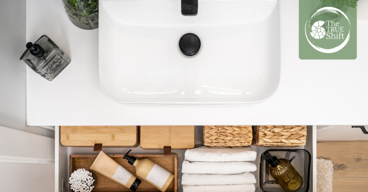 White sink with toiletries and cleaning products on a wooden surface.