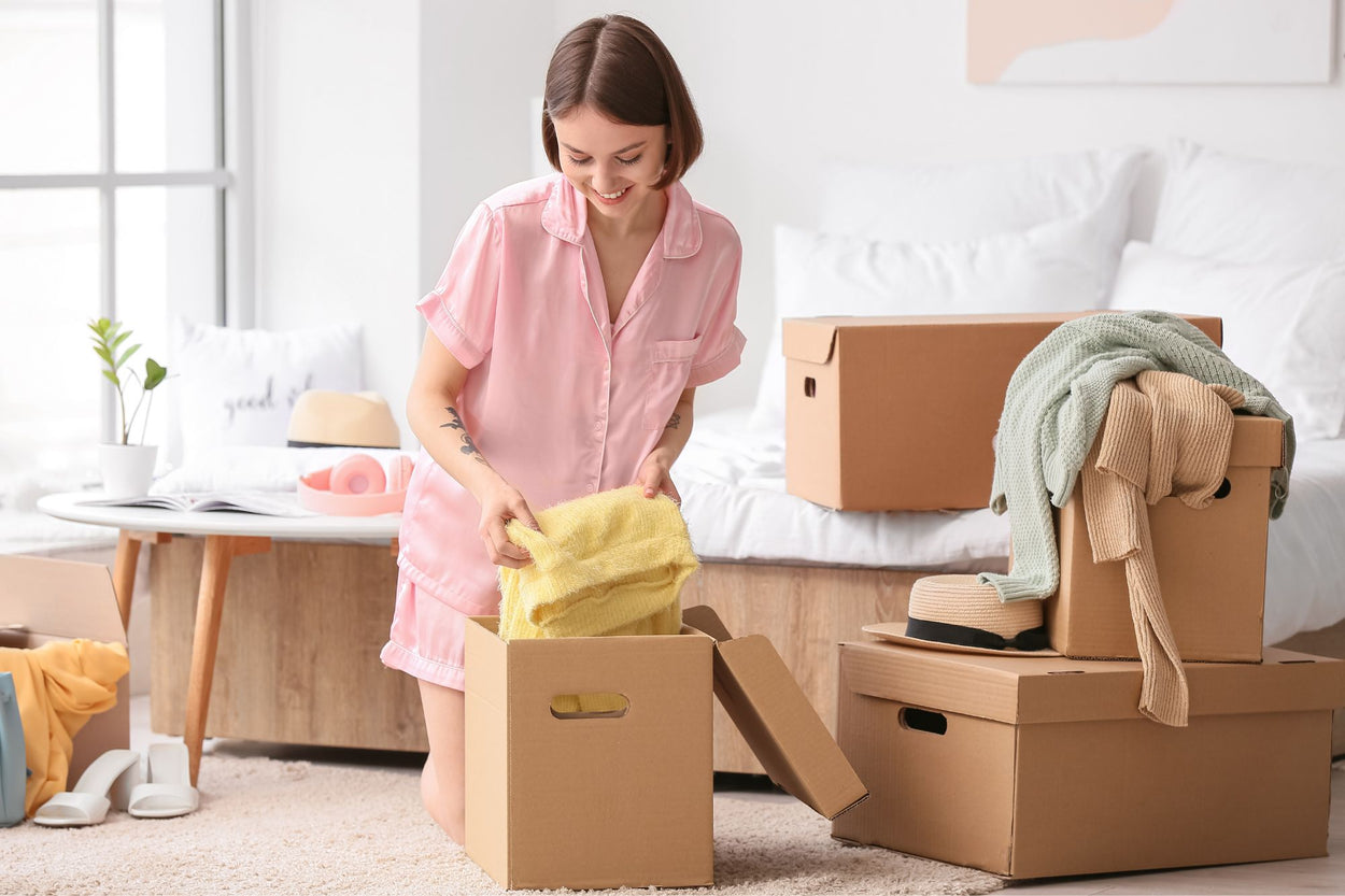 Woman in pink pajamas unpacking boxes in a bedroom.