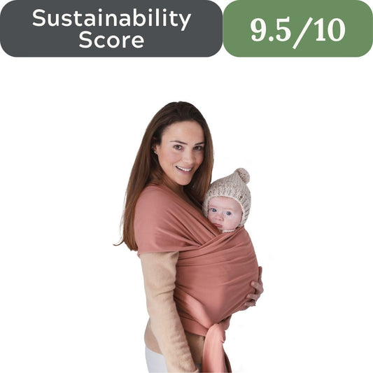 Woman holding a baby in a pink wrap with a 'Sustainability Score 9.5/10' label above. Mushie Organic Cotton Baby Wrap Carrier for non-toxic baby essentials in 2026