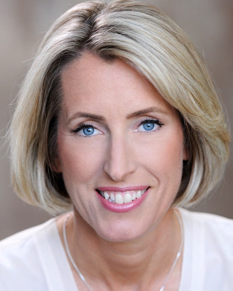 Woman with blonde hair and blue eyes wearing a white shirt against a neutral background