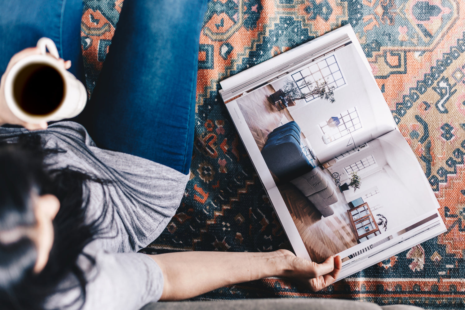 Person holding a coffee mug and an open magazine on a patterned rug